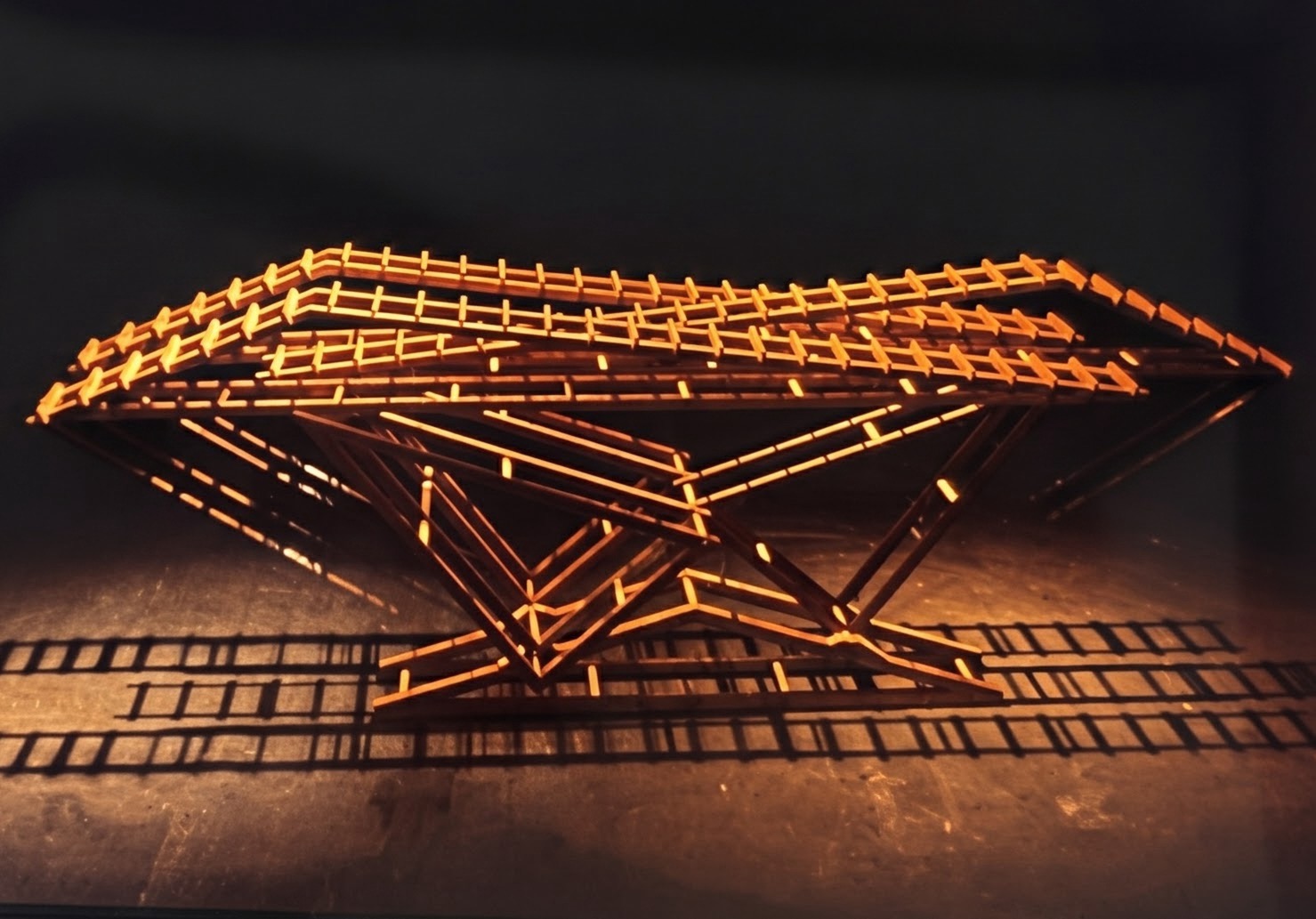 Early horizontal wood and steel sculpture illuminated in warm light on a dark stage