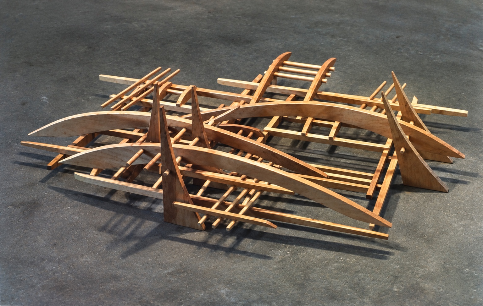 Low wooden sculpture with repeated linear elements and curved forms casting shadows