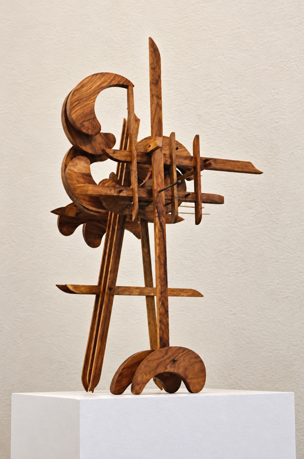 Vertical wooden sculpture with long pointed elements and curling forms on a white pedestal