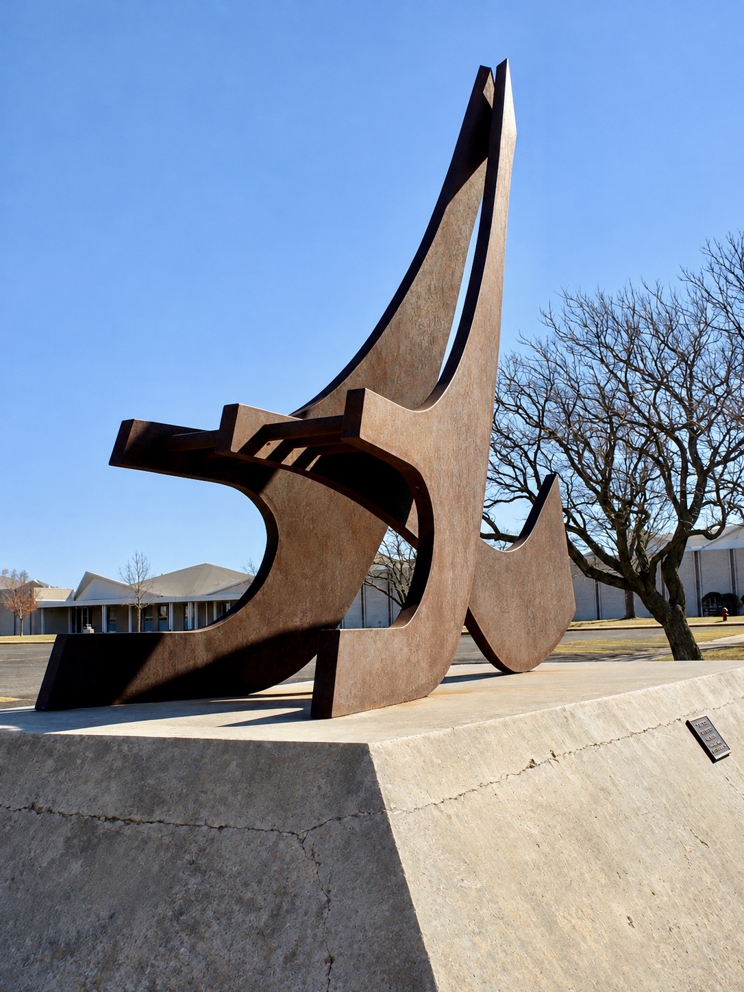 Complete view of a rust-colored abstract steel sculpture on its concrete pedestal
